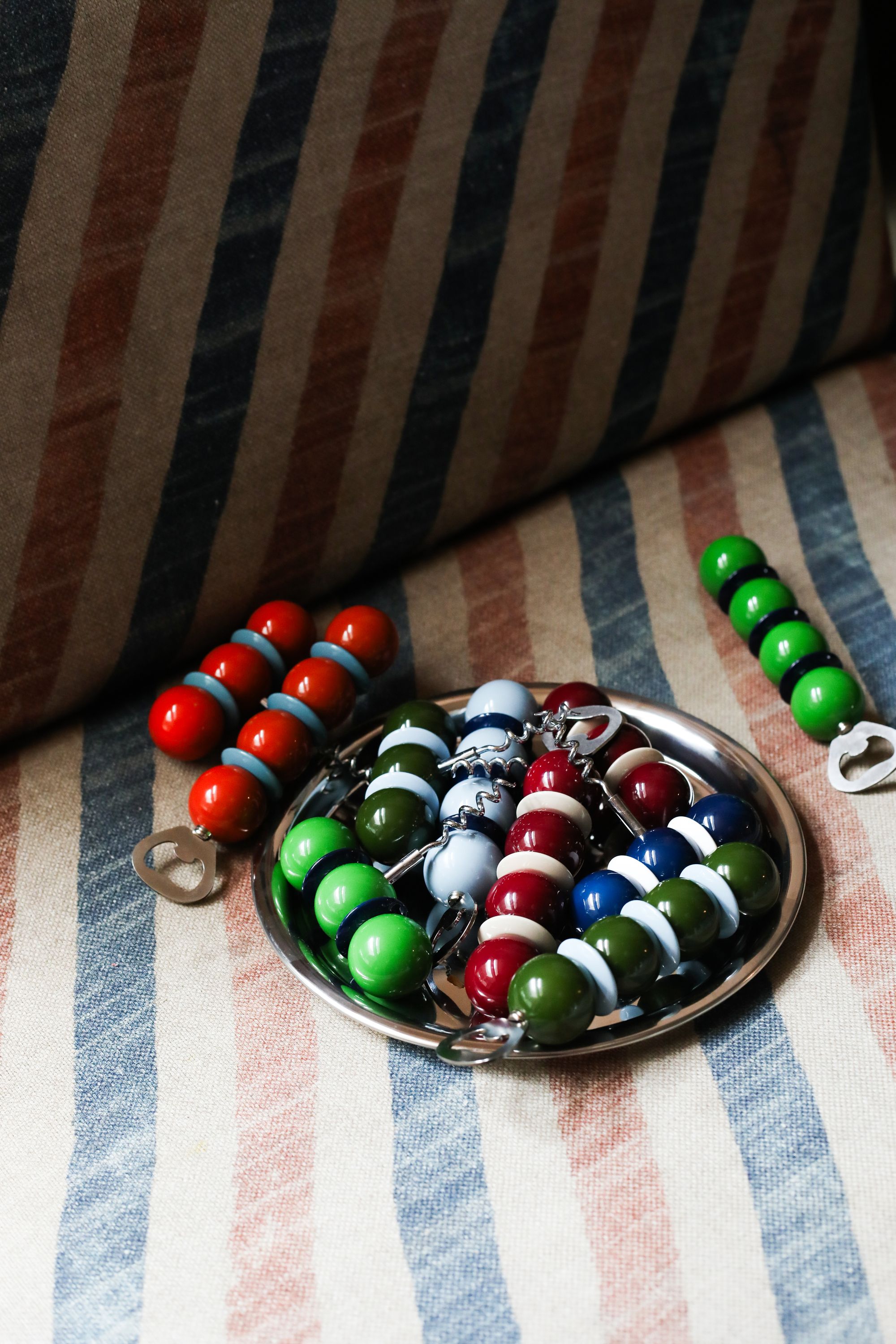 Image of a silver tray with lots of colorful bobbin bottle openers on a red and blue stiped sofa.