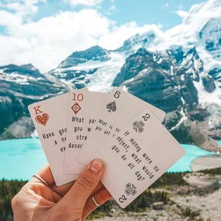 A woman holds Basecamp Cards in front of a backdrop of an alpine lake and mountains