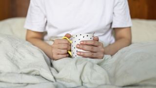 A person holds a mug while sitting in bed