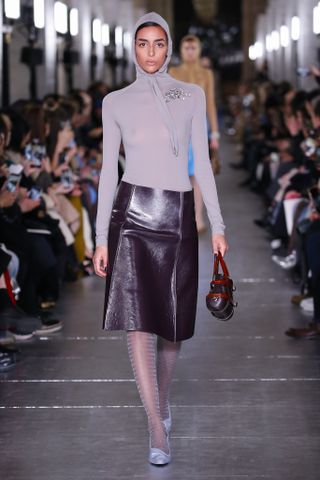 Tory Burch model wears a hooded sweater and leather skirt on the runway