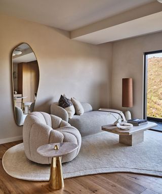 A neutral living room with textured walls, a curved sofa, and a gray area rug