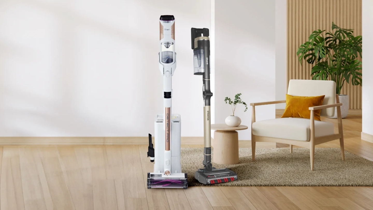 Two vacuums on a floor next to a rug, side table and chair