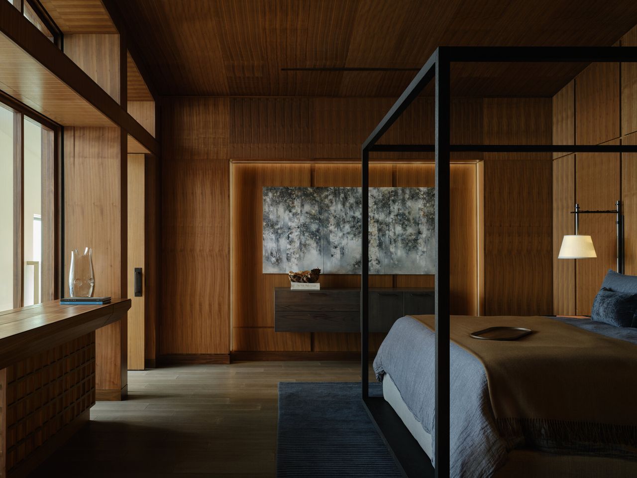 modern timber-drenched bedroom with black four poster bed, a walnut console with artwork above, and a console housing a retractable TV