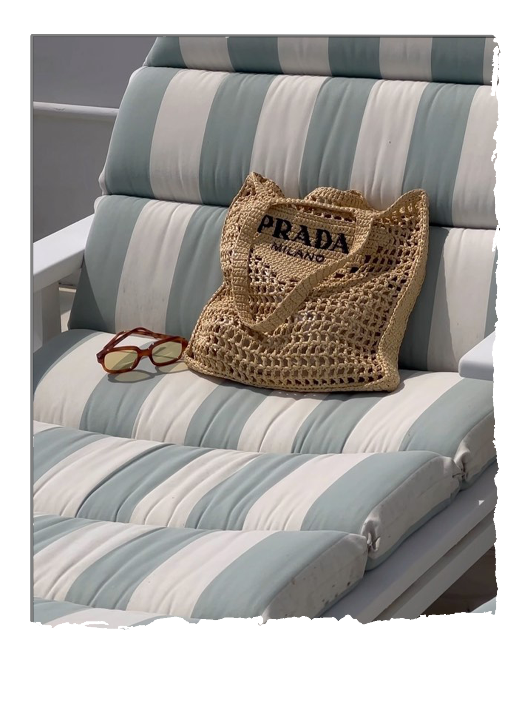@theindiaedit photographs a Prada straw tote bag on a blue-and-white striped sun lounger