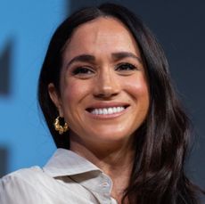 Meghan Markle smiling and wearing gold hoop earrings and a collared blouse 