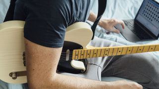 Man watches a video guitar lesson holding an electric guitar
