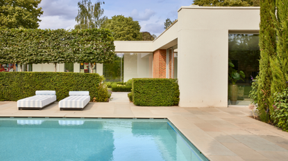 a swimming pool in a paved courtyard garden with two striped sun loungers
