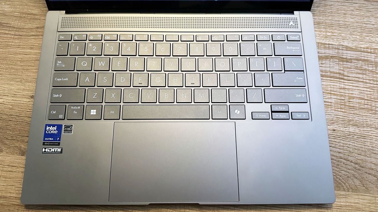 Asus Zenbook S 14 open on a wooden desk showing the keyboard and touchpad.