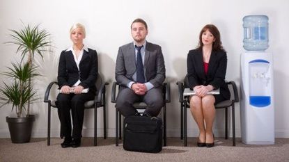 Two women and a man in business attire sitting next to a water cooler.