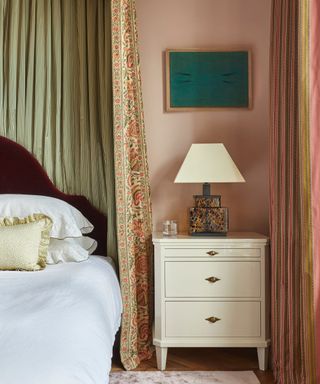 pale pink bedroom with a burgundy velvet headboard, floral drapes, and a teal printed artwork hung above the nightstand