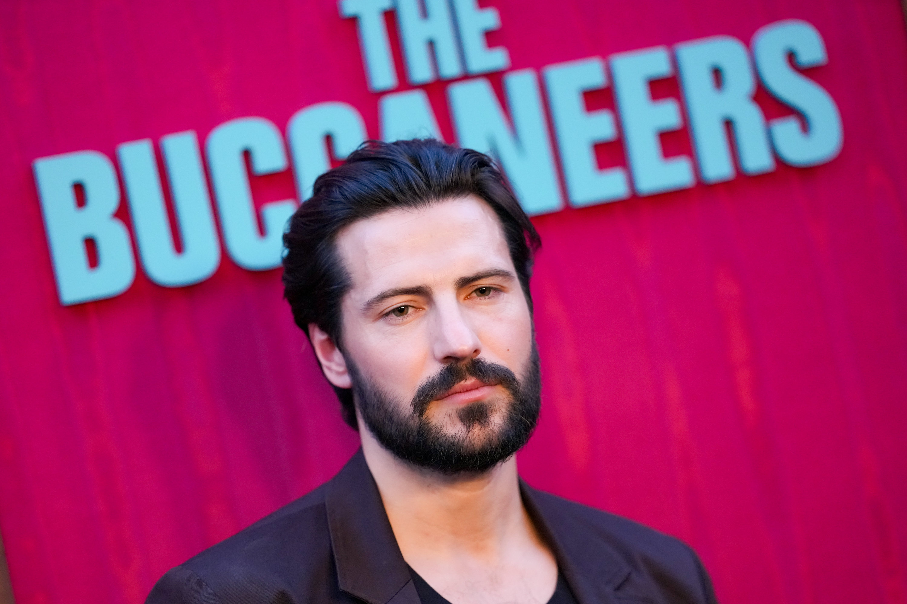 jacob ifran in a black suit on the red carpet at the season 2 premiere of the buccaneers