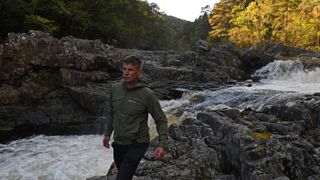 Hiker next to stream wearing a Montane Khamsin Hooded Softshell Jacket