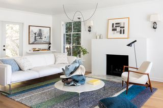 A white-walled living room with large minimalist fireplace and woven blue and grey rug