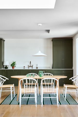 A kitchen diner with green cabinetry, a large oval table, and wooden chairs
