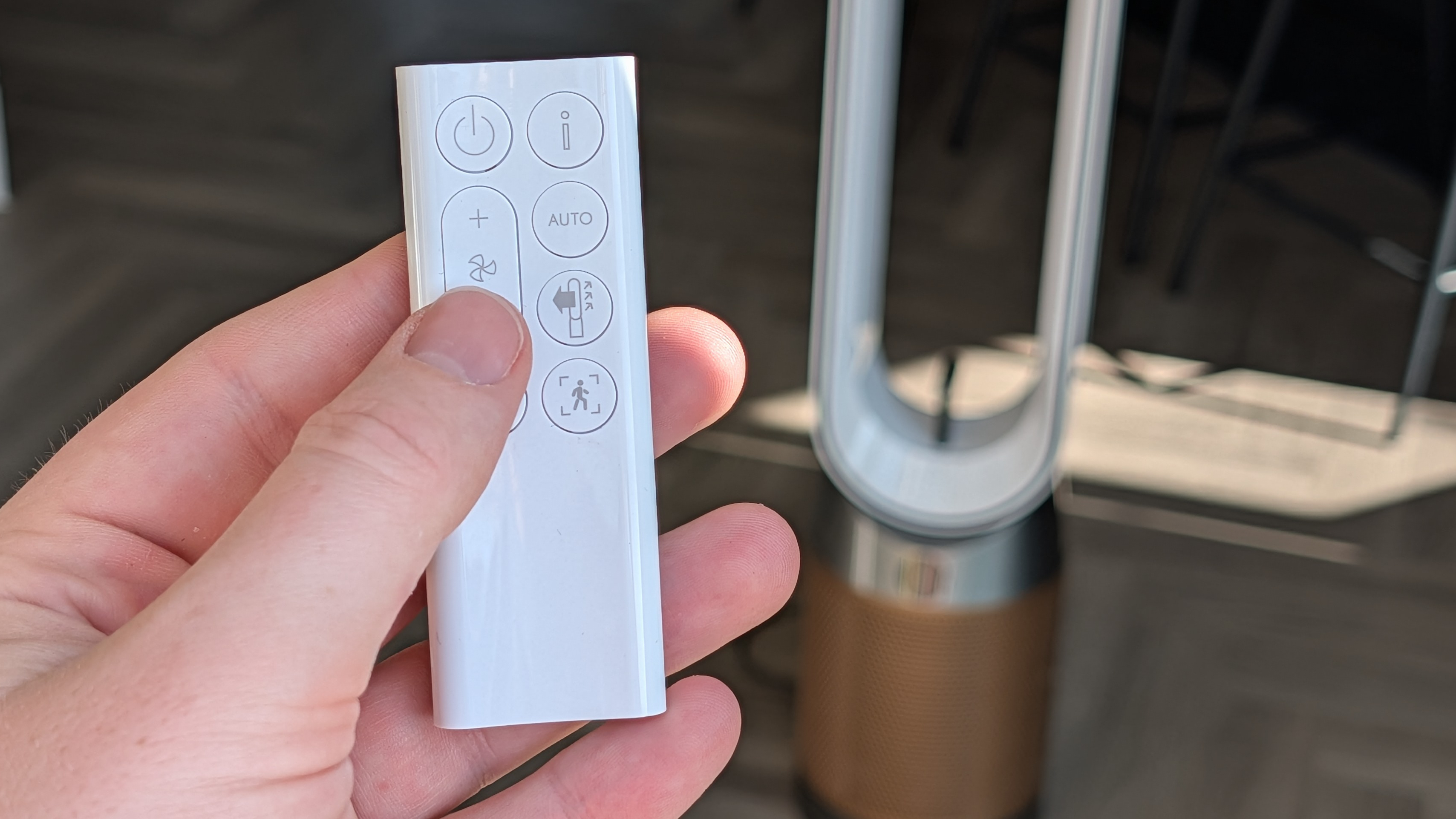 A man's hand adjusting the temperature on the Dyson Find+Follow Purifier Cool's remote, while the air purifier is visible in the background.