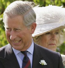 King Charles laughing and Queen Camilla looking serious behind him