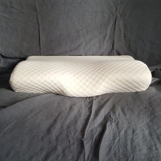 The Kally Sleep Neck Pain pillow being tested on a bed with grey bedlinen