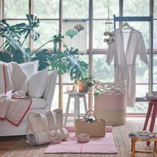 items in the IKEA VÅRDANDE collection, such as a bag, plant pot and blanket, in a light bright living space with huge black crittall windows, a white sofa and a large plant