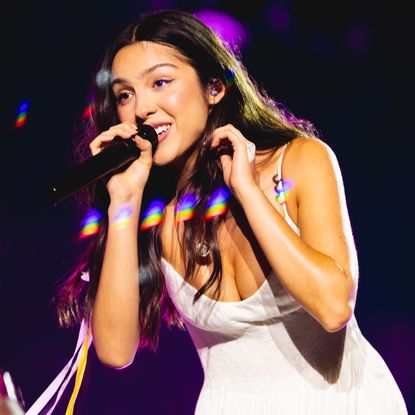 Olivia Rodrigo wears a white lacy dress with a white daisy in her hair to perform at Daisy Chain Fields