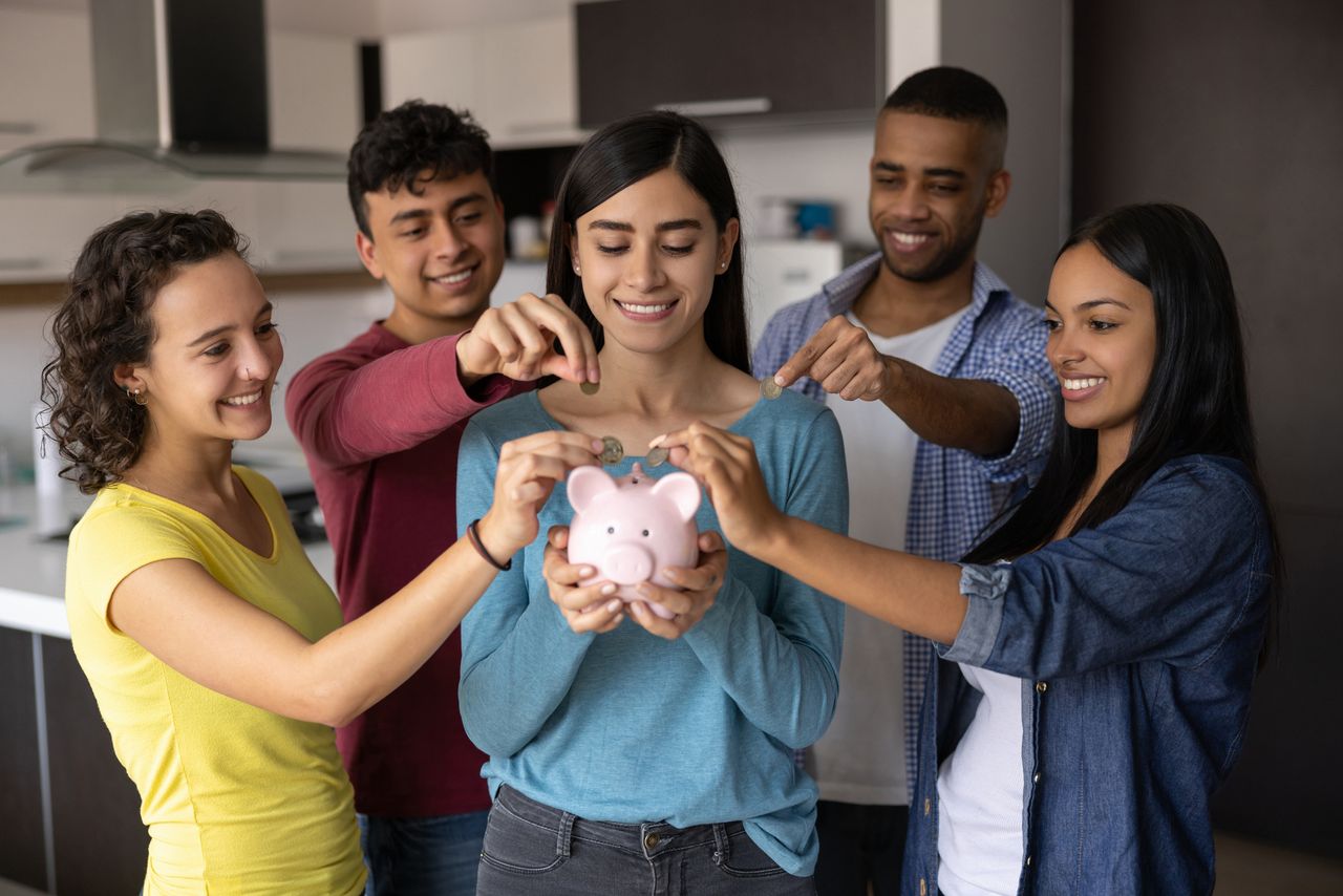 A group of happy friends each putting money into a piggy bank