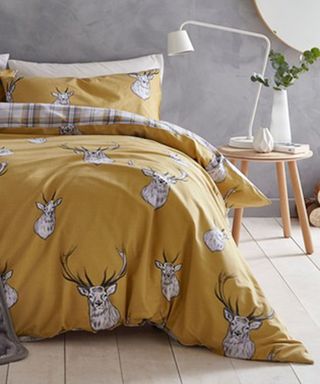 A bedroom with grey concrete-effect wall decor and ocher check and stag motif bedding