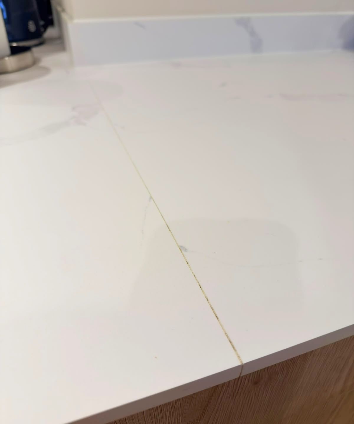 Close-up of white marble-effect worktop with a visible yellowed joint between two sections, above oak-effect units