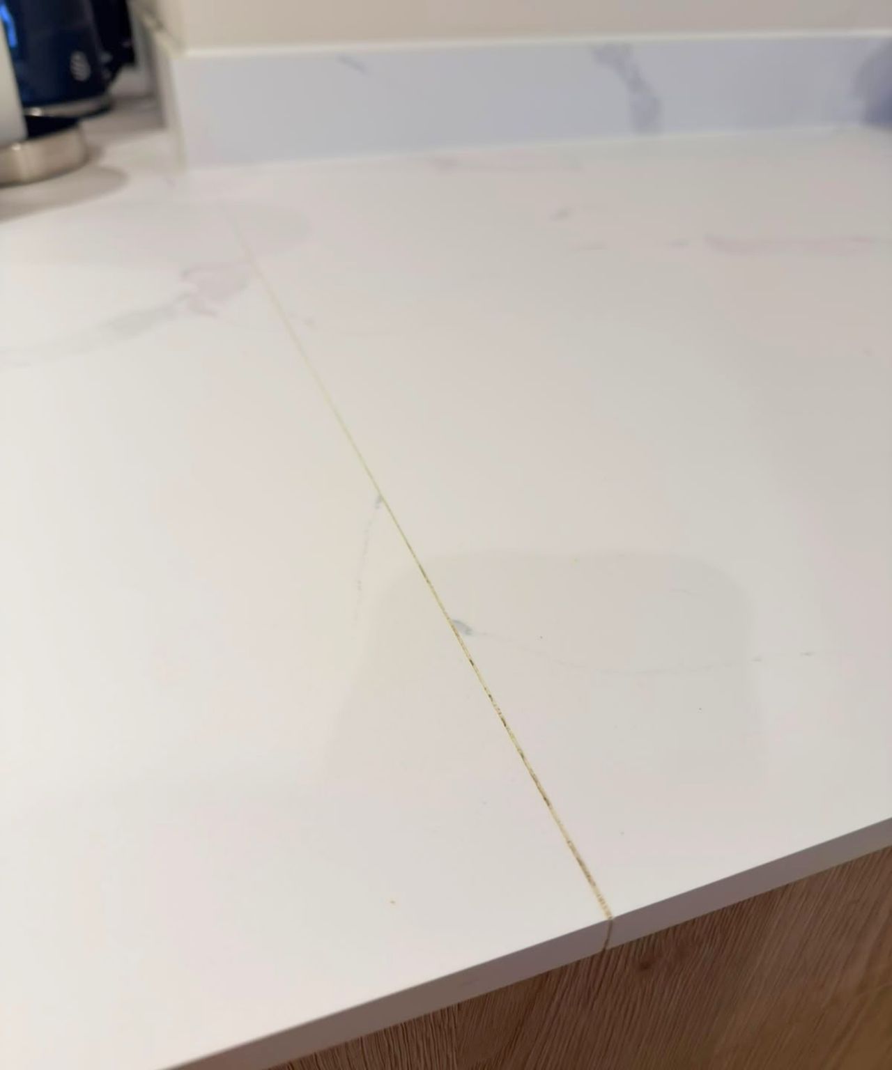 Close-up of white marble-effect worktop with a visible yellowed joint between two sections, above oak-effect units