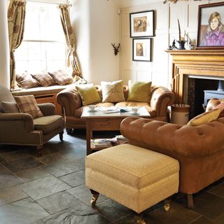 Burnt sienna slate floor tiles in a living room with chesterfield sofas and a wooden fireplace