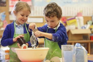Two young children with primary school places baking together in a classroom.