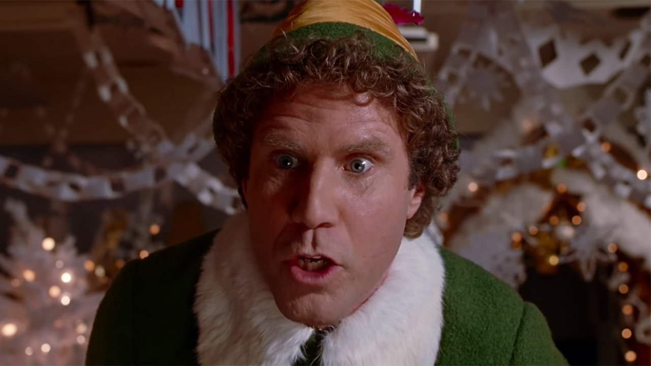 Will Ferrell in green coat and hat yelling at Santa in famous "You Sit On A Throne Of Lies' Elf Scene.