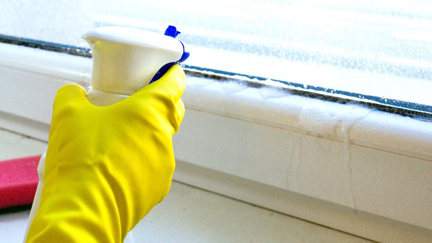 Yellow rubber glove holding a spray bottle spraying cleaner onto UPVC window sealant