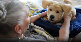 Tombot's robot dog Jennie comforting a senior citizen and raising its ears after being petted