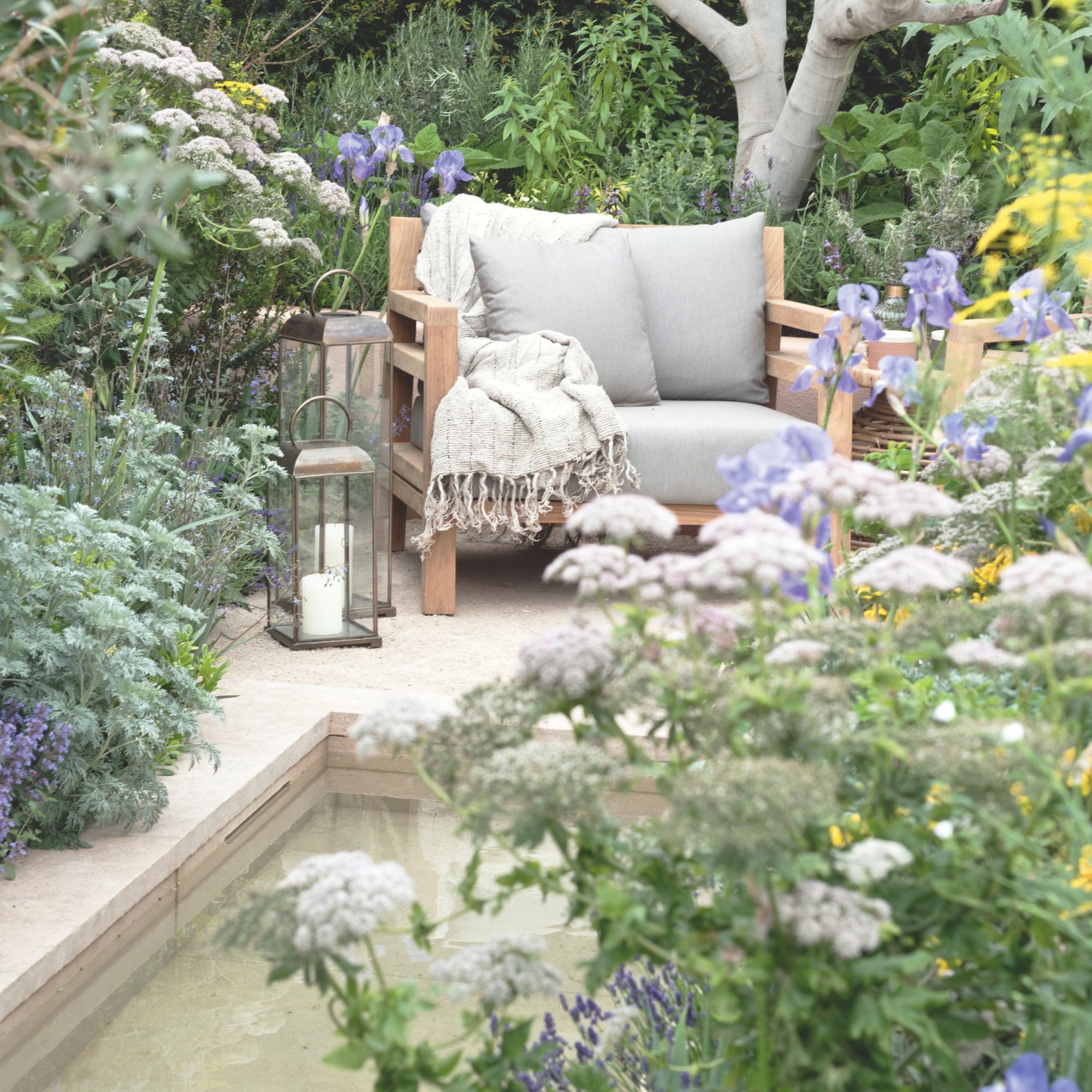 A seating nook in a garden with a water feature in front, surrounded by plants 