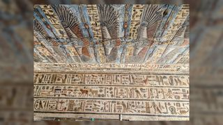 Ancient Egyptian temple ceiling decorated in colorful frescoes. The ceiling itself looks like it's covered in vulture-like creatures. The walls are covered in Egyptian hieroglyphs.