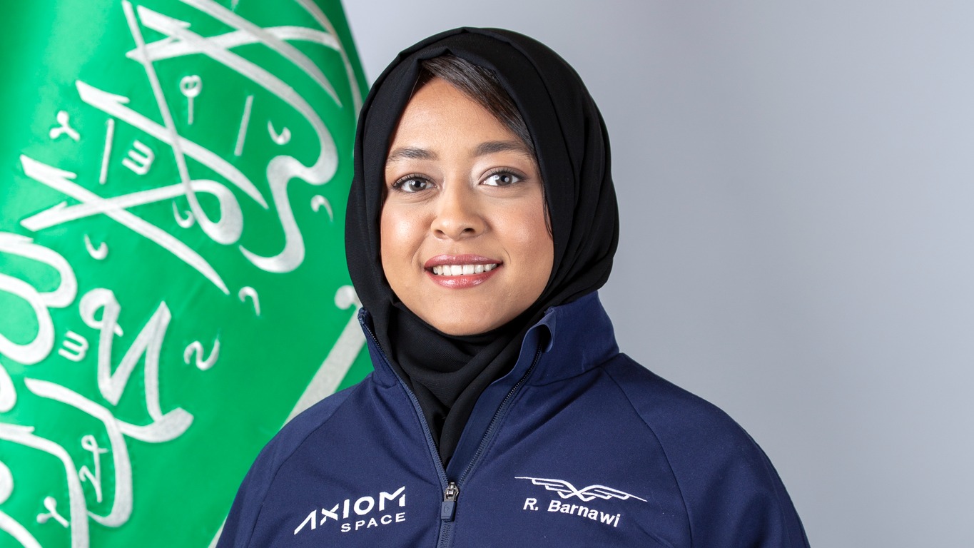 portrait of Rayyanah Barnawi in an Axiom spaceflight suit next to a flag with Arabic script