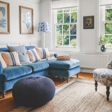 White painted living room with a bright blue sofa and round pouffe on the floor in front of it, on a jute rug