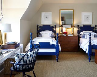 Twin guest room with cobalt blue single beds featuring spindle bedposts, and dressing table laden with everyday essentials, spindle chair and floral blue cushion.