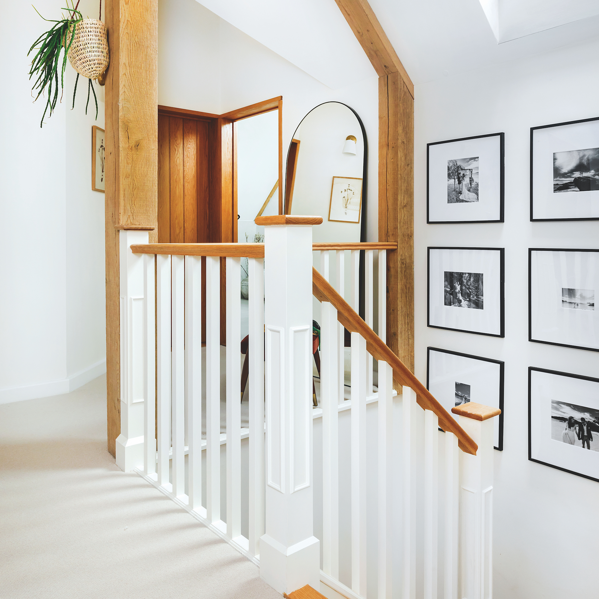 landing of oak frame house with white painted stair spindles and cream carpet with black and white photographs on wall
