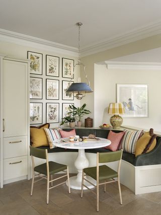 kitchen with dining nook with green velvet seating and mustard and pink cushion and artwork with round table