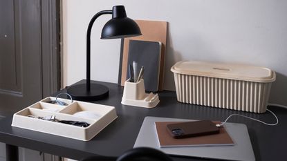 IKEA HÖNSNÄT cable management box on a black desk with a black lamp, notebook, phone and other organisers 