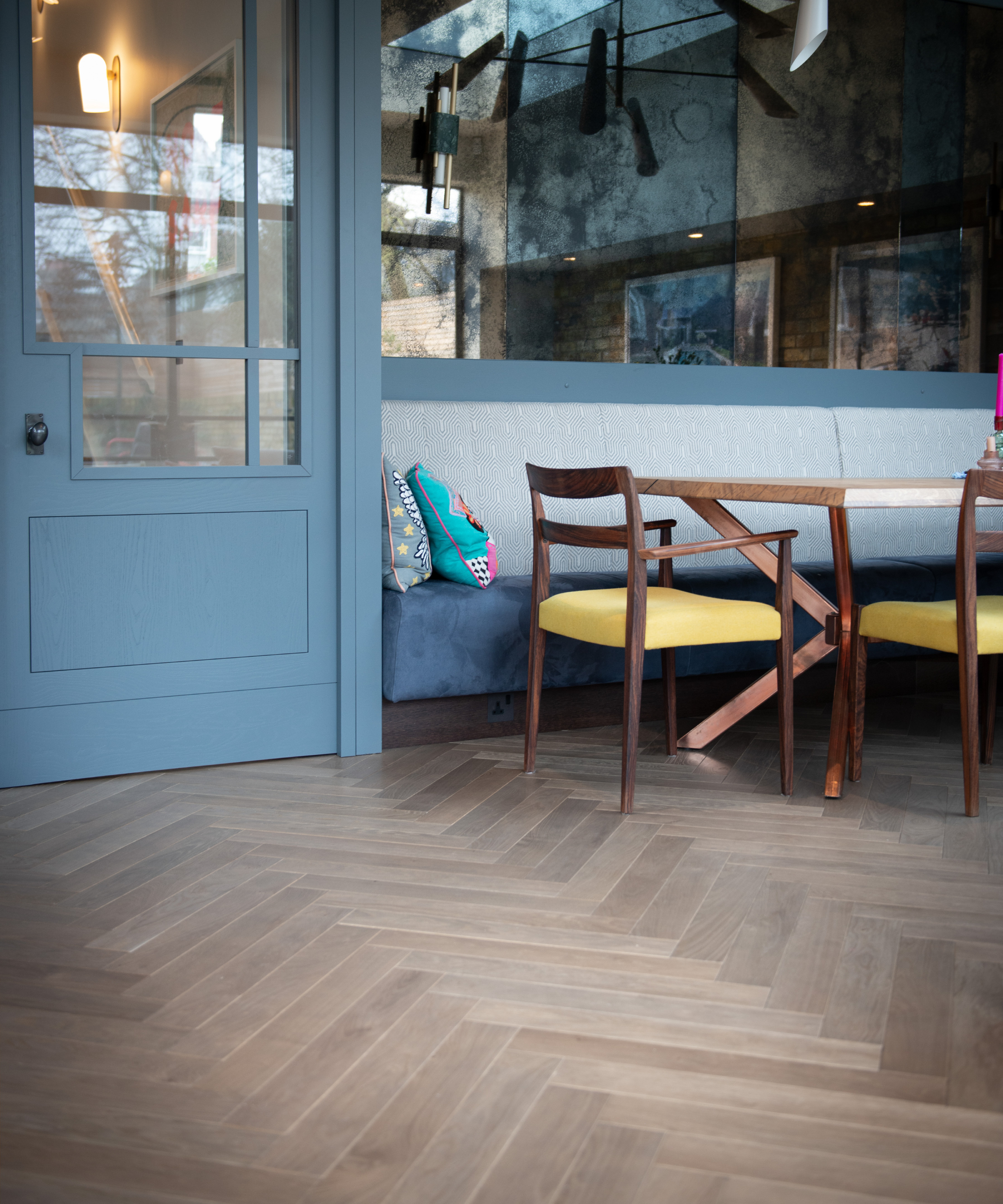 walnut herringbone wooden floor, blue banquette seating, wooden table and chairs and blue and glass door