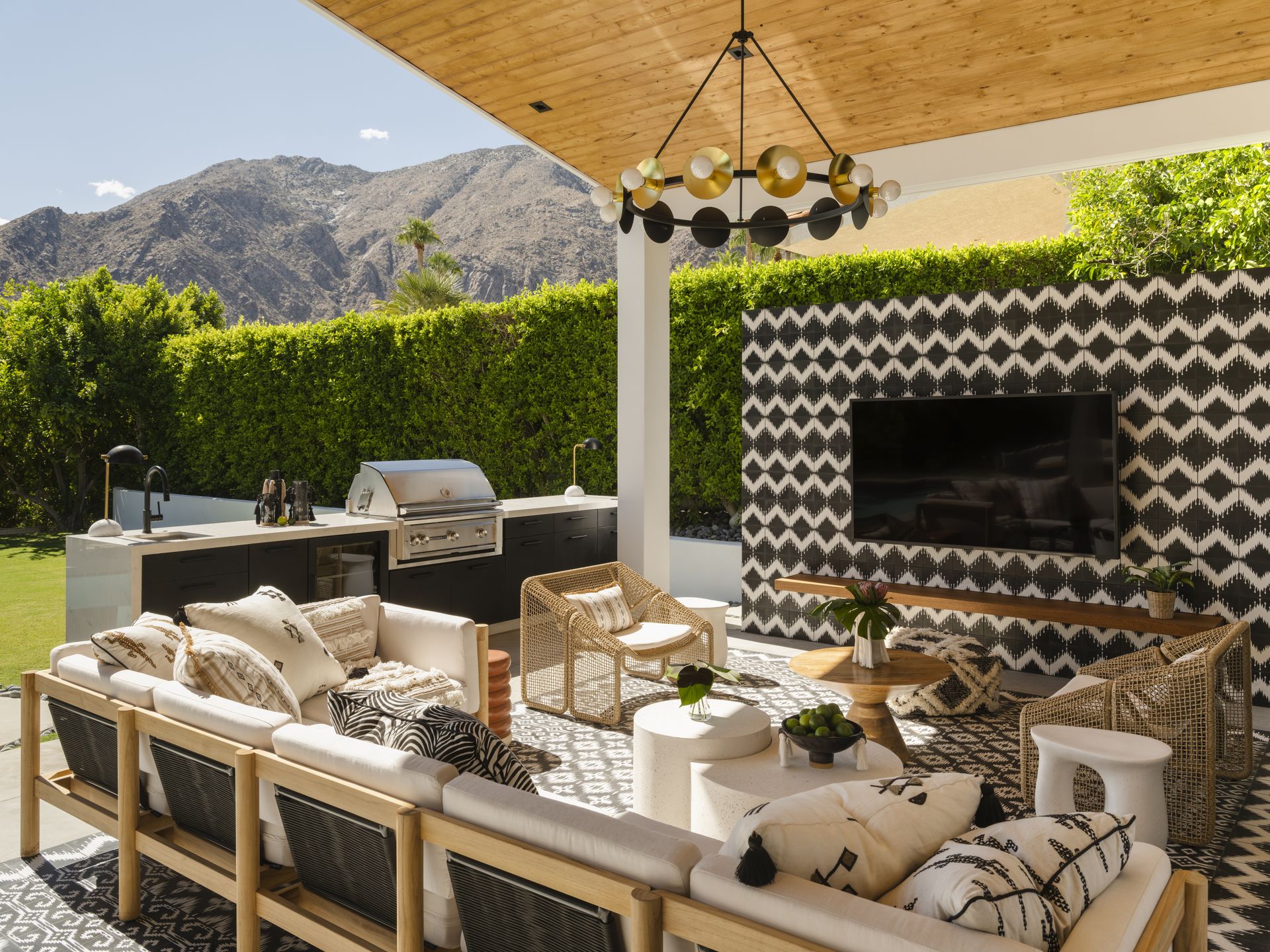 An outdoor space with seating and a chandelier, a tiled wall complete with outdoor tv, bbq area in the garden, and a view of the mountains in the background