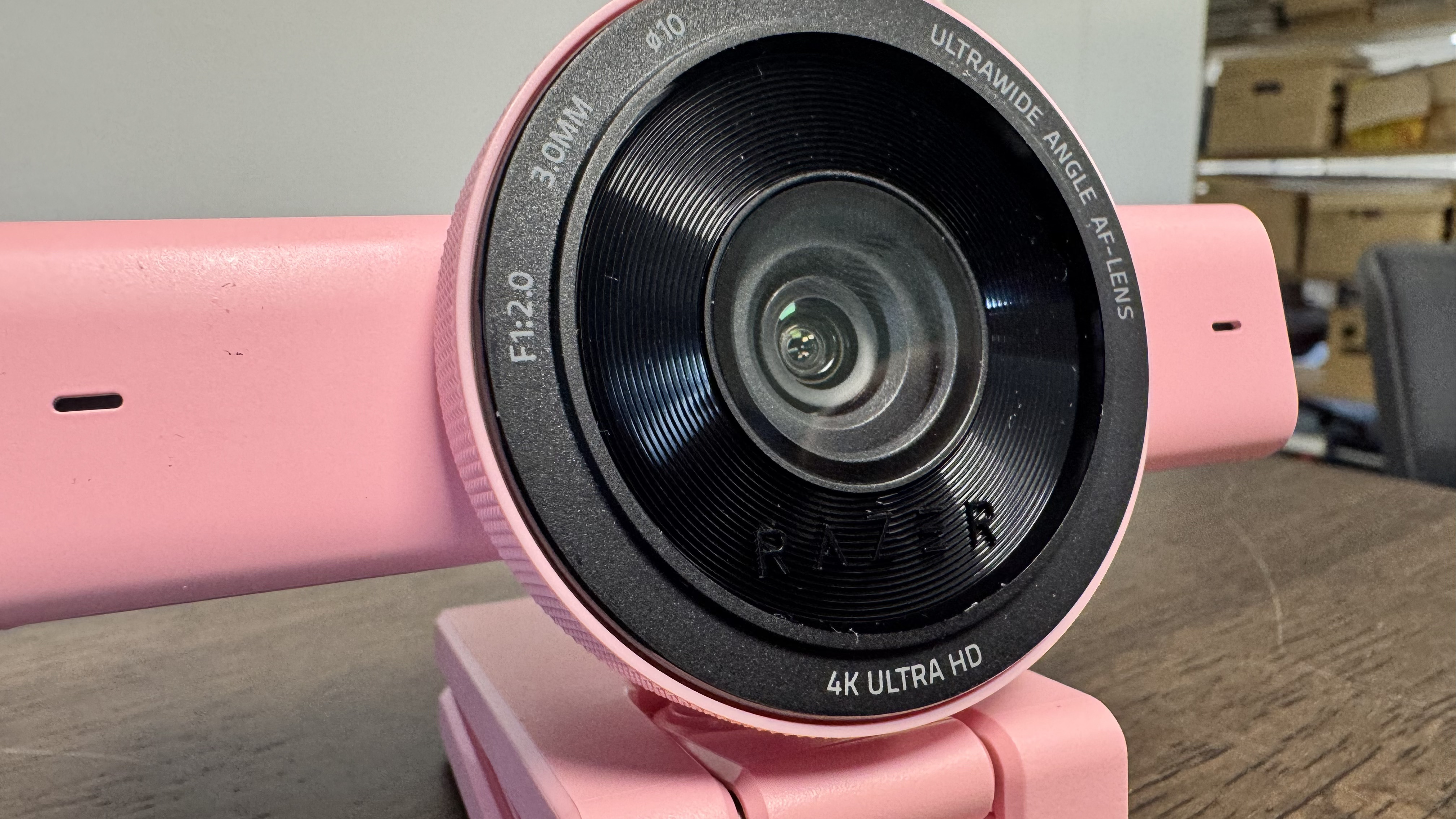 The pink Razer Kiyo V2 from the front right, on a wooden desk, up close