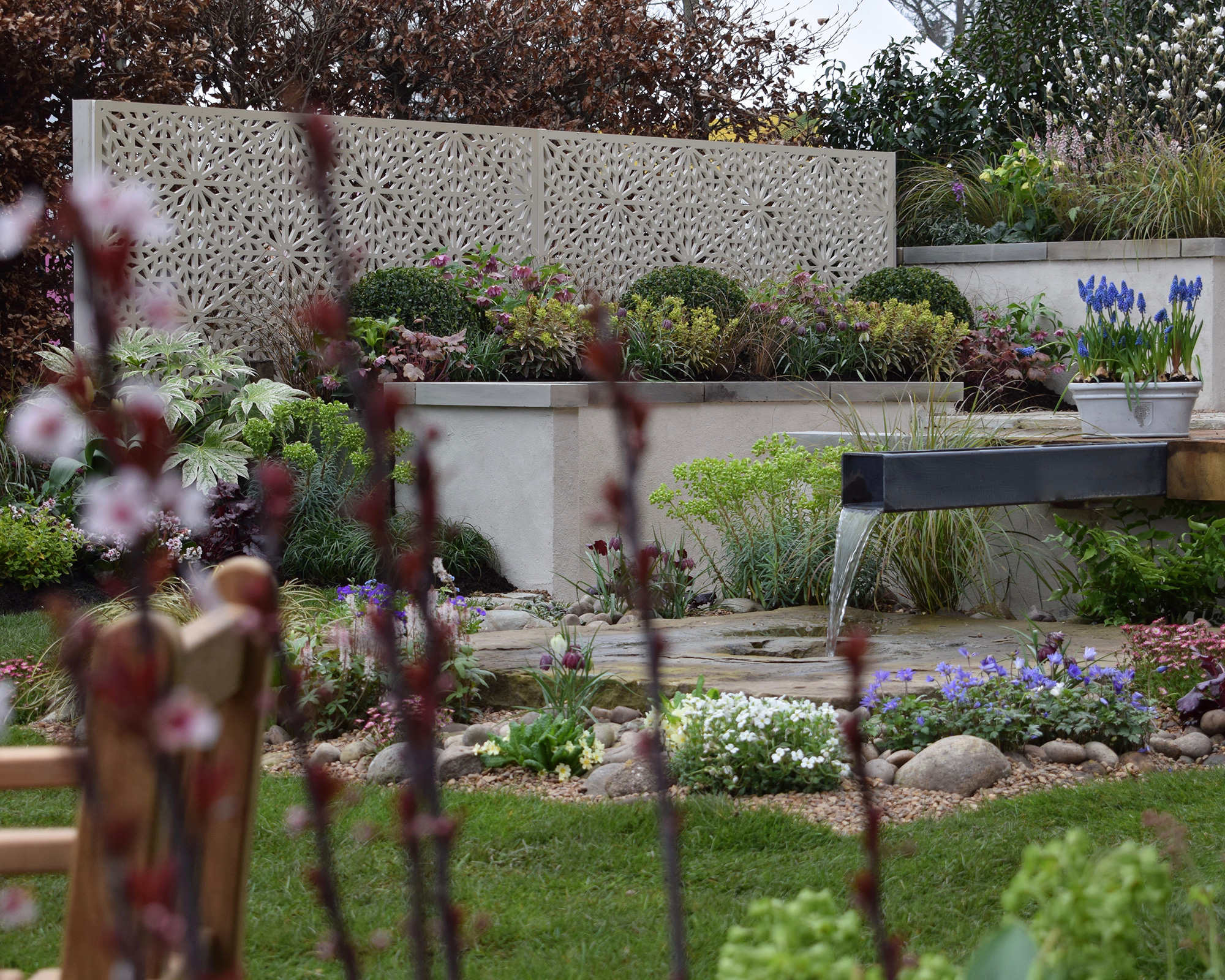 A lush garden with colourful flowers, manicured bushes and a patterned privacy screen