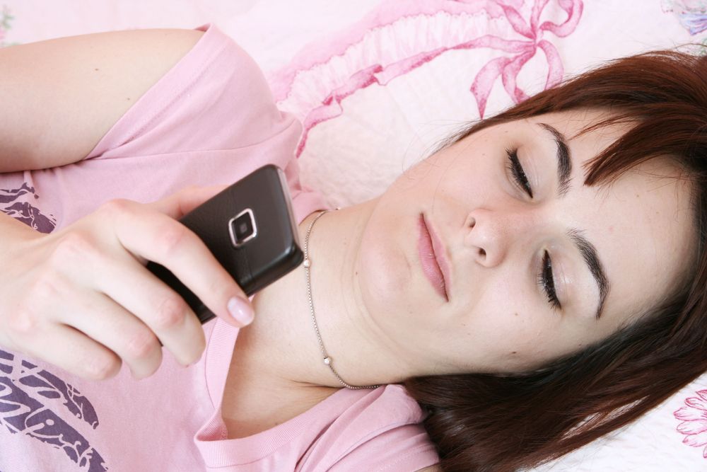 A woman uses her cell phone in bed.