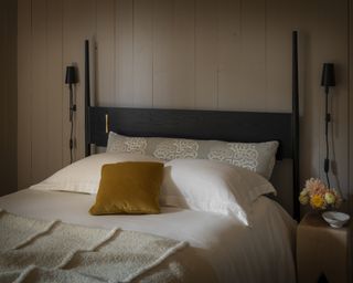 A bedroom with white shiplap walls and a black and brass postered bed