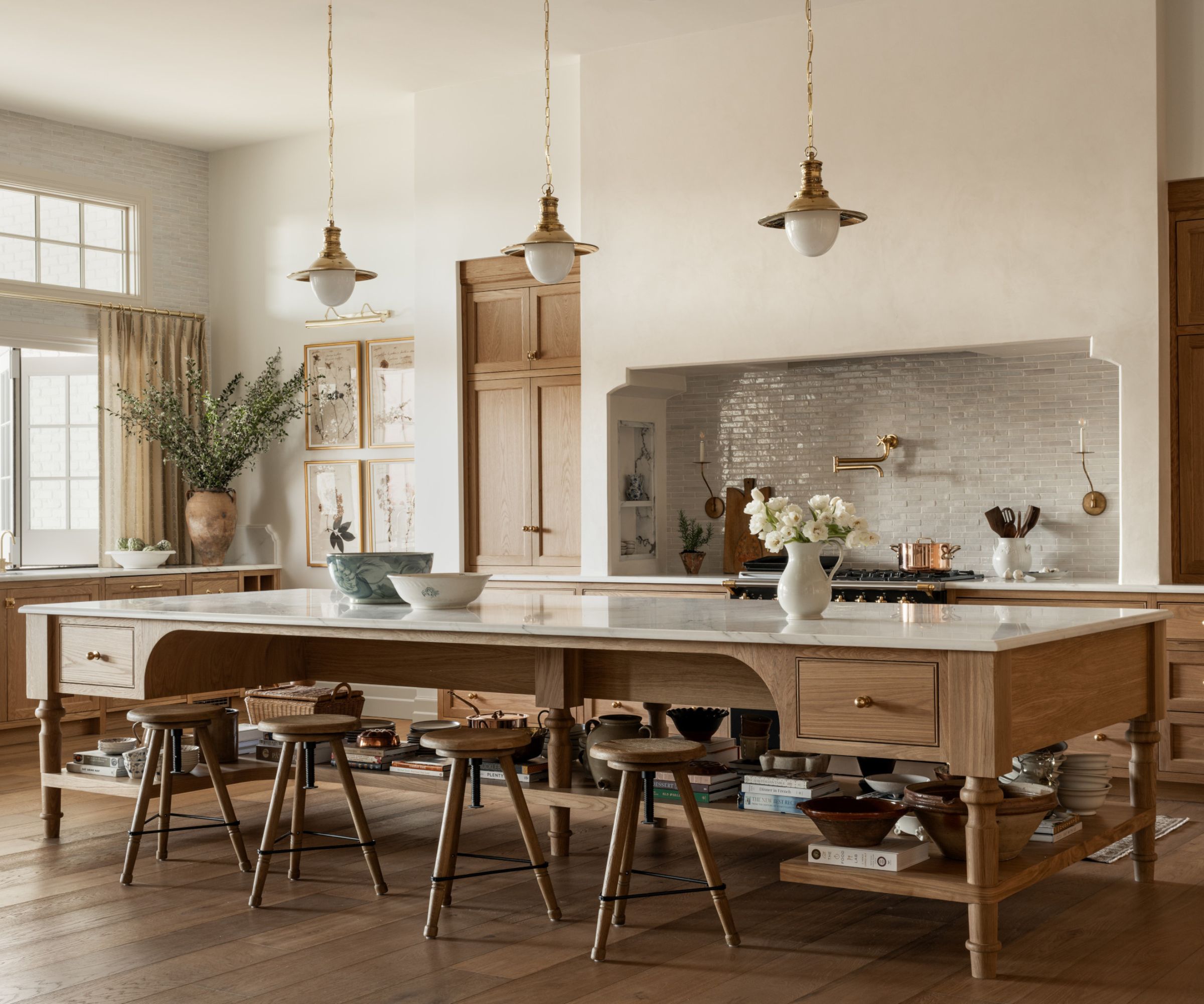 A large kitchen with wooden cabinets, marble countertops, brass accents, and a large wooden freestanding island