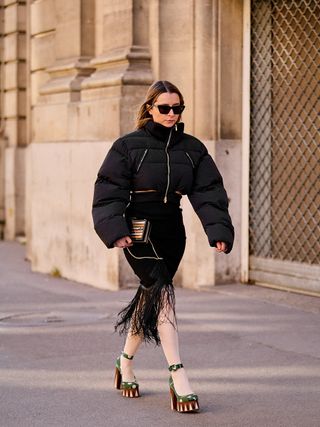 best down jackets, woman wearing black crop puffer with fringe skirt and platforms