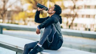 Man drinking protein shake sitting on a wall after a workout