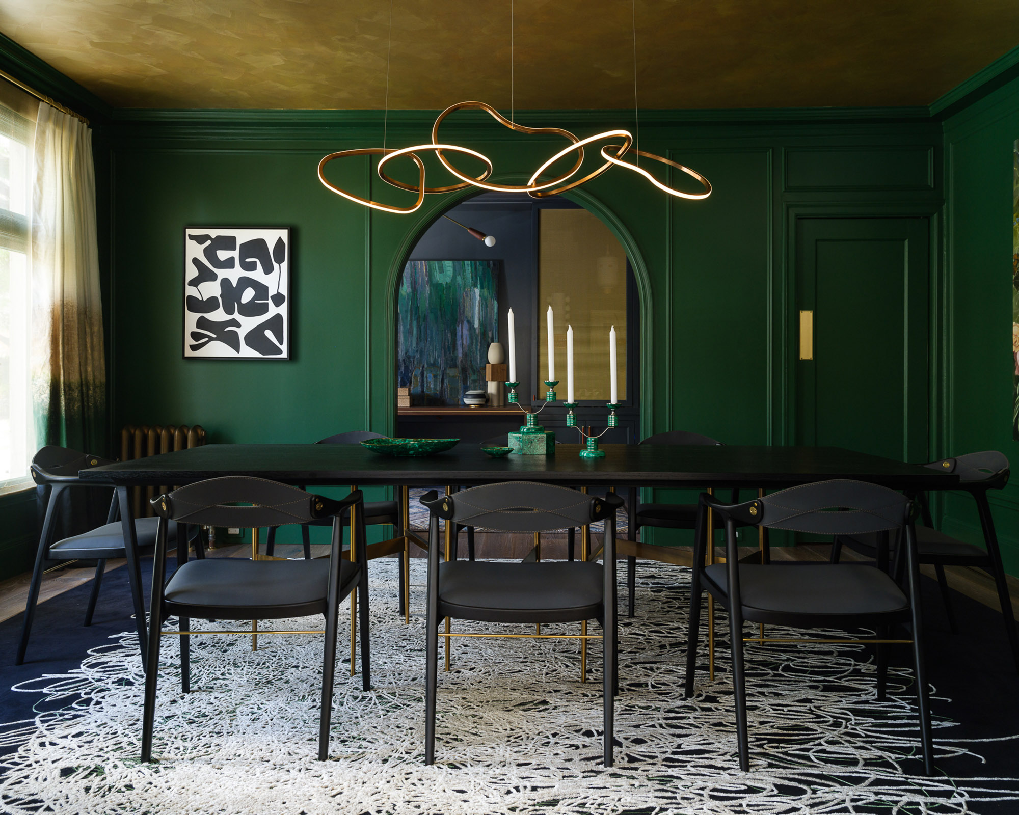green dining room wiht black table and large gold ceiling light hanging over it